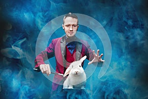 Magician shows trick with disappearance white rabbit in suitcase magic wand, black background photo