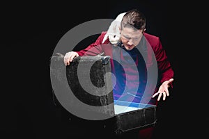 Magician shows trick with disappearance white rabbit in suitcase magic wand, black background