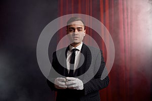 Magician wearing suit standing with cane on stage decorated red velvet curtain