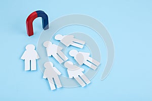 Magnet attracting paper people on blue background