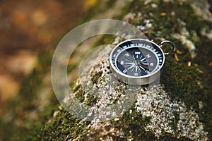 Magnetic compass with a black dial on a wild stone covered with green moss. The concept of finding the way and