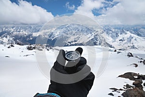 Magnetic compass in a man's hand in a black glove against the background of the snow-capped mountains of the caucasus in