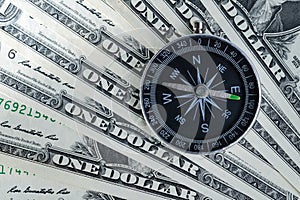 Magnetic compass on pile of dollar bills usning as world economics fortune direction