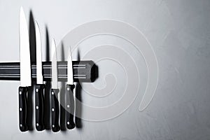 Magnetic holder with set of knives on grey stone background