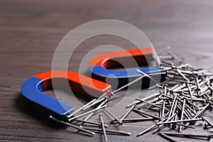 Magnets attracting nails on grey wooden background, closeup