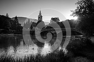 Black and white picture of sunrise over Bohinj lake with Church of St John the Baptist on the lakeside, Bohinj, Slovenia, Europe