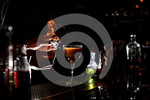 Magnificent close-up of bartender`s hands lighting a flame near glass with cocktail.