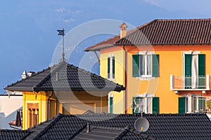 Magnificent Italian facade of residential building with shutter windows and tile brown roof in sun light near mountain