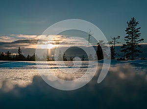 Magnificent photo of vertical light orange Sun beam shining from behind of heavy clouds down to pine tree forest. Winter snowy