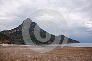 magnificent view from beach shore to mountain with green trees on it and cloudy sky