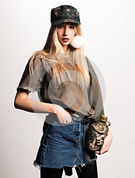 Magnificent white girl in military clothes posing with flask. Studio portrait of beautiful lady in jeans skirt looking