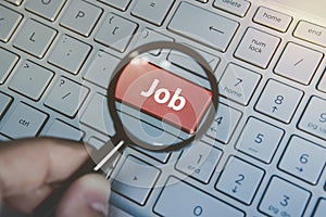 Magnified through the loupe job button on keyboard of a laptop. Man uses magnifying glass to enlarge job key on computer