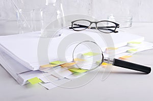 Magnifier against stack of documents, medical glassware, glasses on the white laboratory desk