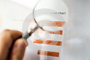 Magnifier on a coloured funnel chart printed on a white sheet of paper during a business meeting