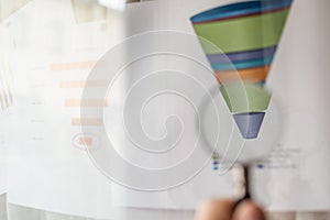 Magnifier on a coloured funnel chart printed on a white sheet of paper during a business meeting