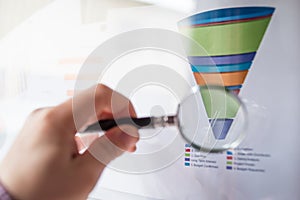 Magnifier on a coloured funnel chart printed on a white sheet of paper during a business meeting