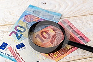 Magnifier on euro banknotes over a white wooden surface. Check the authenticity of money. Wealth, poverty and counterfeiting money