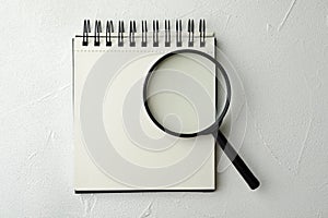 Magnifier glass and empty notebook on white background, flat lay with space for text. Find keywords concept