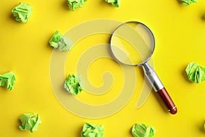 Magnifier glass and green crumpled paper sheets on yellow background. Find keywords concept