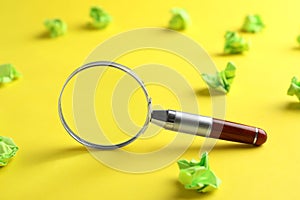 Magnifier glass and green crumpled paper sheets on yellow background. Find keywords concept