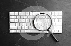 Magnifier glass and keyboard on black background, flat lay. Find keywords concept