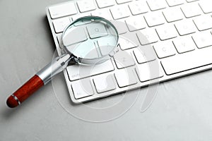 Magnifier glass and keyboard on grey stone background, closeup. Find keywords concept