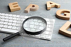 Magnifier glass, keyboard and letters on grey wooden table, closeup. Find keywords concept