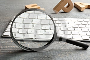 Magnifier glass, keyboard and letters on grey wooden table, closeup. Find keywords concept