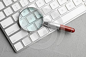 Magnifier glass and keyboard on grey stone background, top view. Find keywords concept