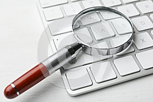 Magnifier glass and keyboard on white table, closeup. Find keywords concept