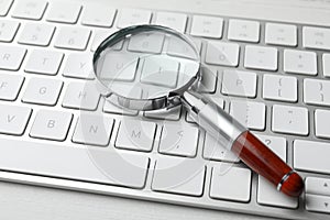 Magnifier glass and keyboard on white table. Find keywords concept