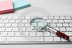 Magnifier glass and keyboard on white table. Find keywords concept