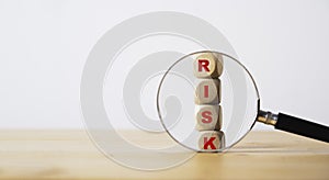 Magnifier glass with red risk wording on wooden block cubes for focus risk analysis assessment and management concept