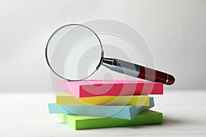 Magnifier glass and stack of colorful memory stickers on white table. Find keywords concept