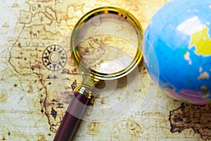 Magnifier and globe on old map background.