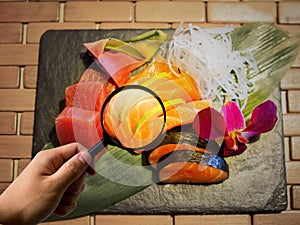 Magnifier on sashimi mix types of fish on stone plate, calories and clean food concept