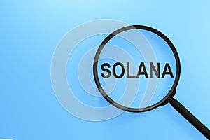 Magnifier written with text SOLANA on a blue background. Business and cryptocurrency concept