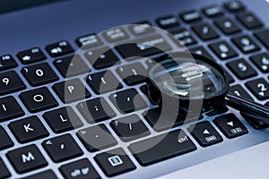 Magnifyer glass on laptop computer keyboard in blue tone,