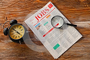 Magnifying glass with alarm clock and newspaper on wooden background