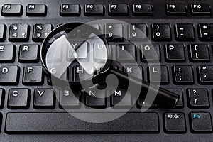 Magnifying glass on the black computer keyboard closeup. Find keywords and online resources, network search, Internet security