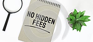 A magnifying glass, a blank brown notebook on a white table. NO HIDDEN FEES sign