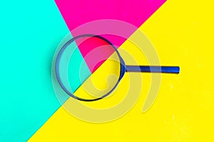 Magnifying glass on bright geometric green, red and yellow background.