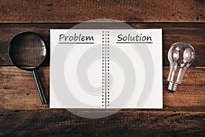 Magnifying glass, bulb and notebook written PROBLEM and SOLUTION with copy space on wooden table