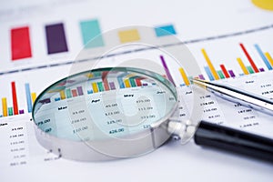 Magnifying glass on charts graphs spreadsheet paper.