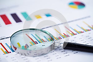 Magnifying glass on charts graphs spreadsheet paper.