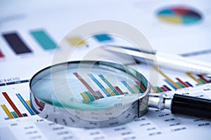 Magnifying glass on charts graphs spreadsheet paper.