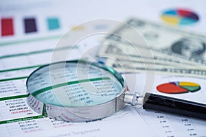 Magnifying glass on charts graphs spreadsheet paper.