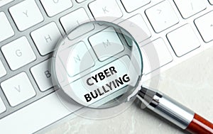 Magnifying glass and computer keyboard with phrase CYBER BULLYING on white button