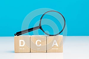 Magnifying glass and DCA word on a wooden cube in idea Dollar Cost Averaging investment strategy, Saving stock or savings on a