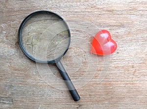 magnifying glass and decorative red hearts isolated on a brown wooden background minimalist trend.valentines day concept